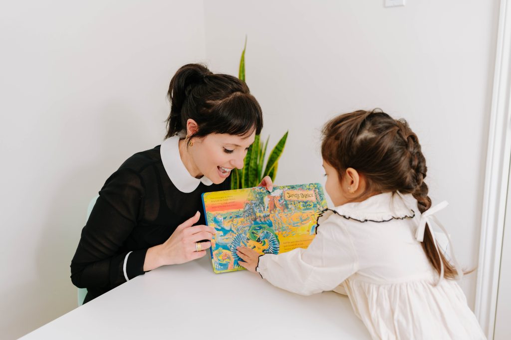Speech language pathologist providing engaging pediatric speech therapy to a toddler using a picture book, available in-home or online